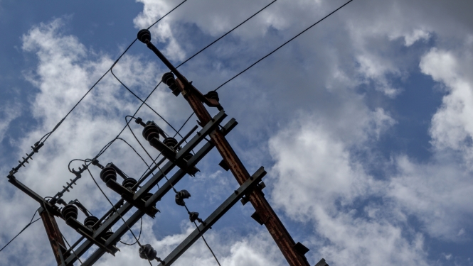 Zilas debesis ar mākoņiem, vienā malā redzams elektrības stabs
