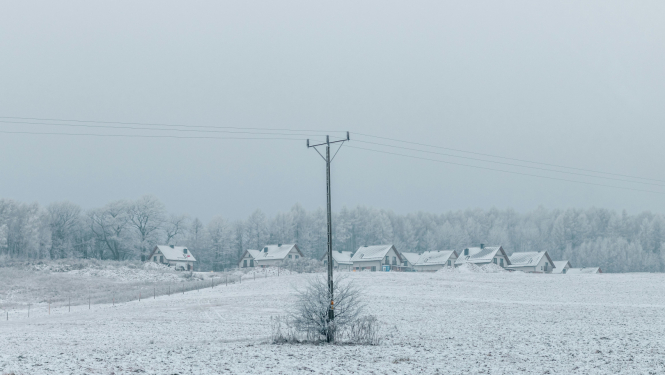 Ziemas ainava ar apsnigušām privātmājām un elektrības līniju priekšplānā