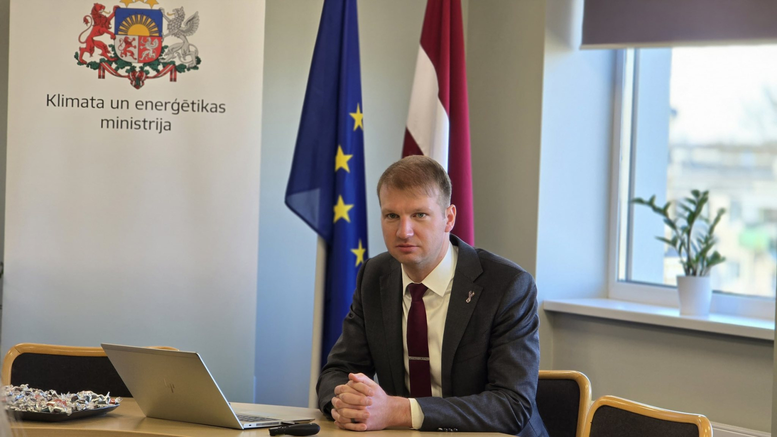 Ministrs Kaspars Melnis - portrets, fonā redzams Latvijas un ES karogs un ministrijas logo