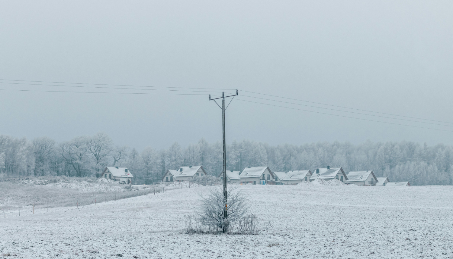 Ziemas ainava ar apsnigušām privātmājām un elektrības līniju priekšplānā